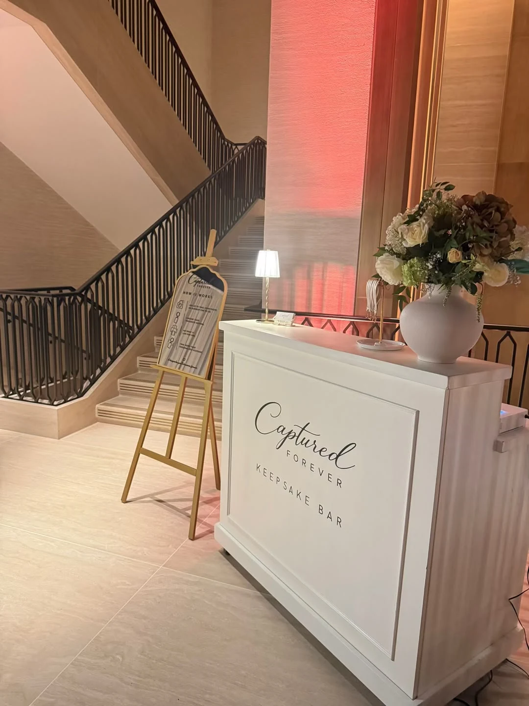 The Captured Forever Keepsake Bar styled with flowers beside a hotel staircase
