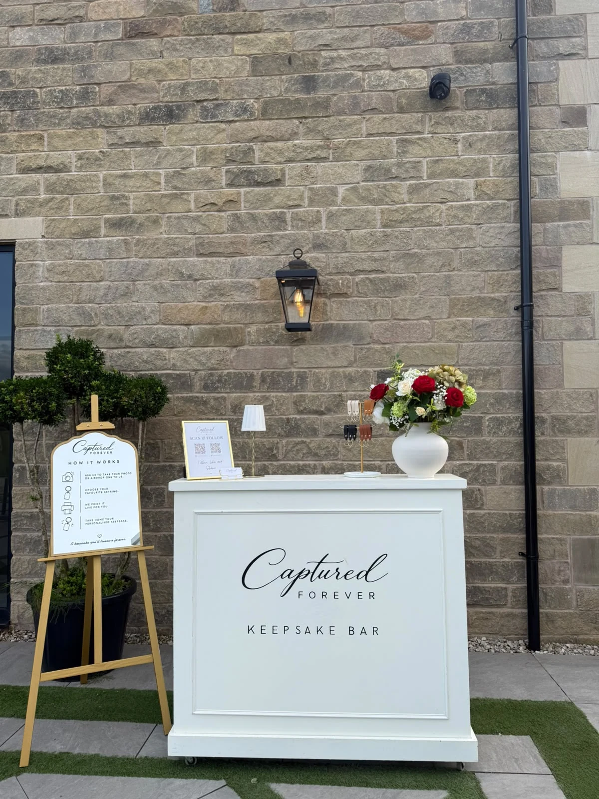 Front view of the Captured Forever Keepsake Bar and How It Works easel at an outdoor event