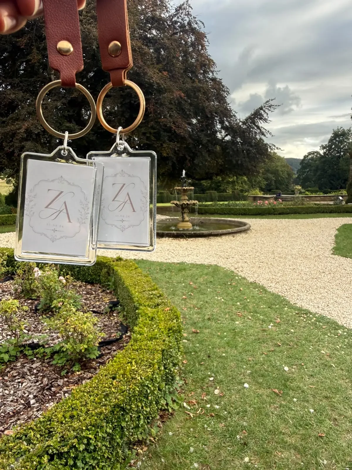 A pair of personalised leather keyrings displaying an event monogram in a formal garden