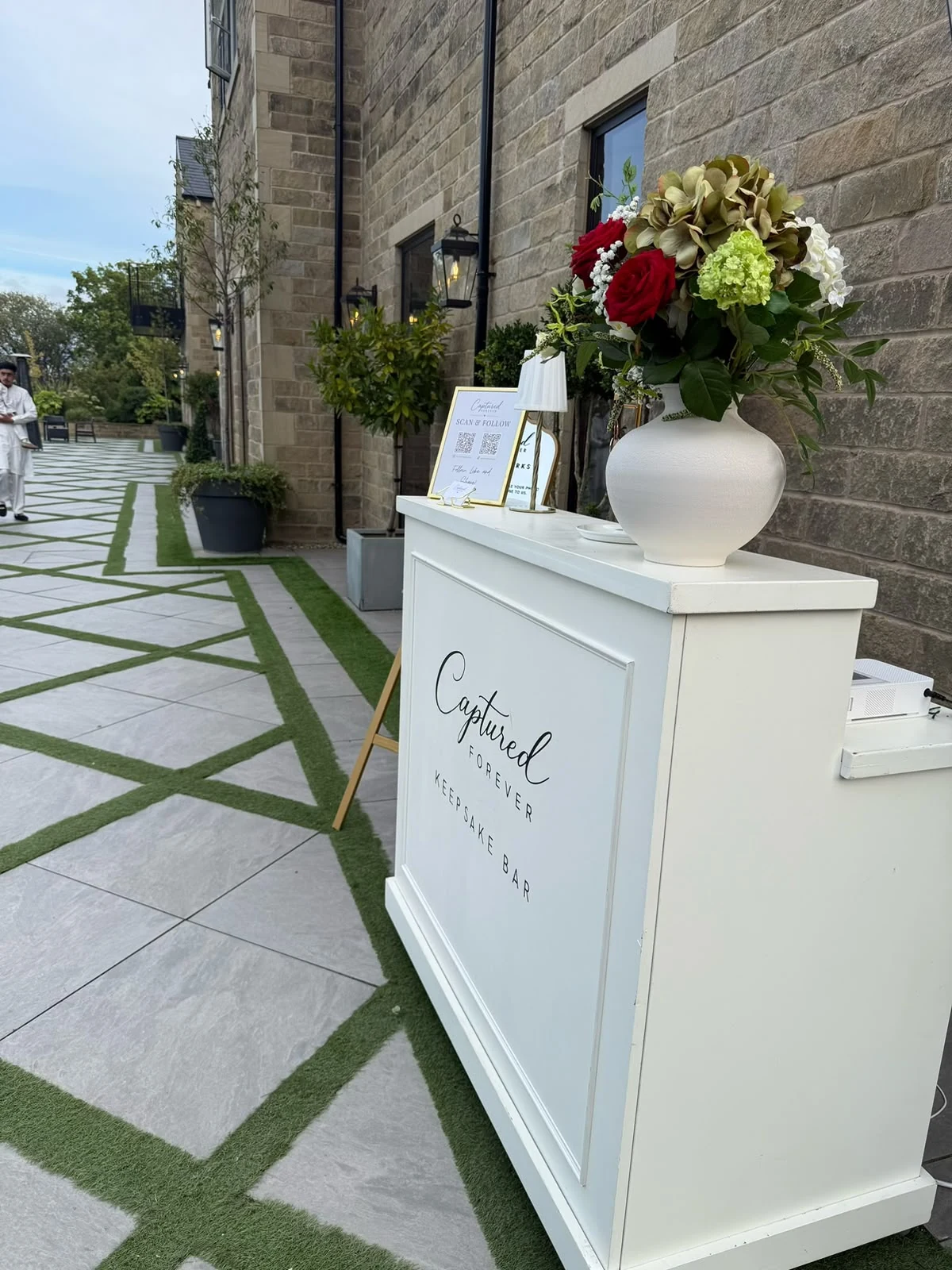 The Captured Forever Keepsake Bar arranged outdoors beside a stone venue with floral styling