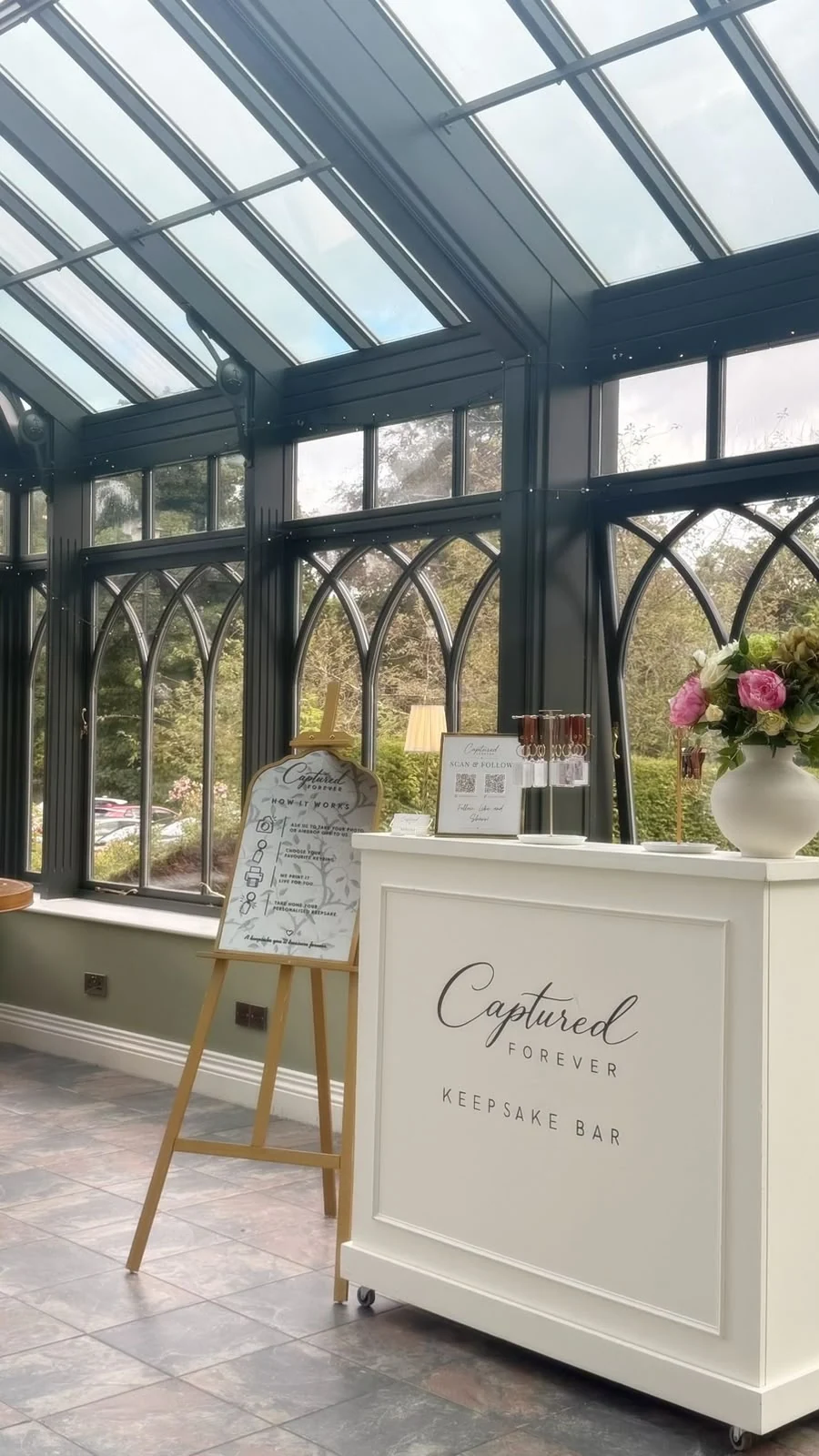 The Captured Forever Keepsake Bar set beneath the tall windows of a glasshouse venue