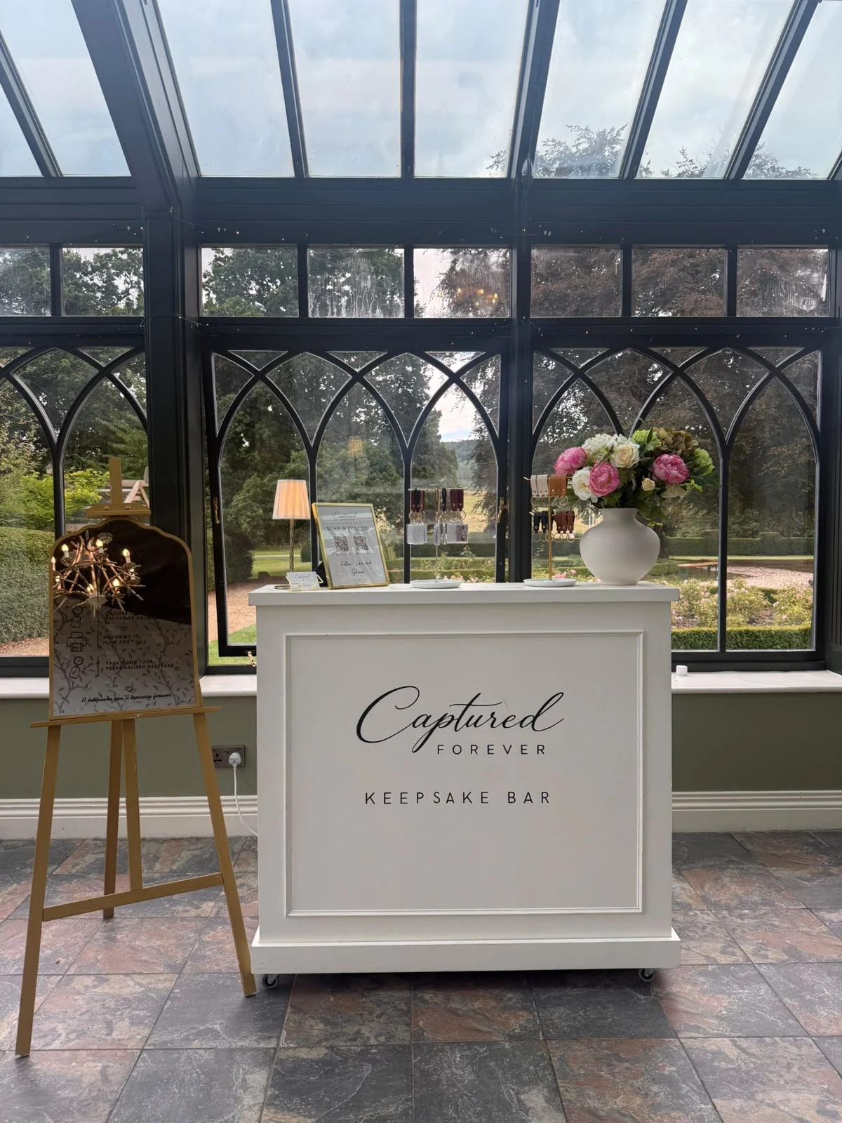 Front view of the Captured Forever Keepsake Bar beneath the arched windows of a glasshouse venue