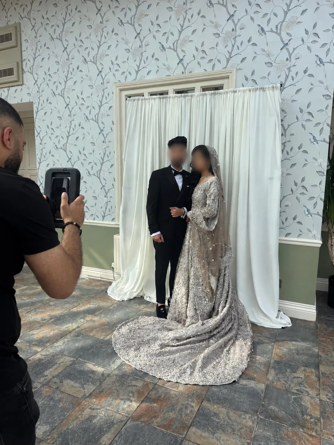 A couple having their portrait taken in front of the Keepsake Bar photography backdrop